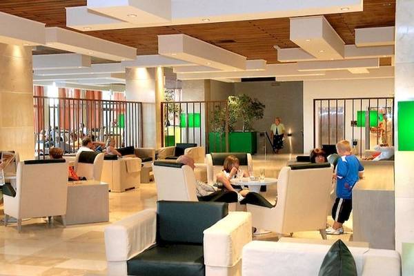 Lobby des Atlantica Nissaki Beach Hotels mit Gästen, die auf weißen Sesseln sitzen und lesen.