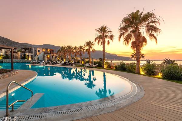 Der Swimmingpool des Ikaros Beach Luxury Resort & Spa bei Sonnenuntergang mit Loungeliegen und Palmen