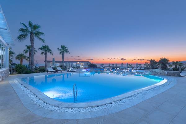 Außenpool des Ikaros Beach Luxury Resort & Spa bei Sonnenuntergang mit Lounge-Bereich und Palmen.