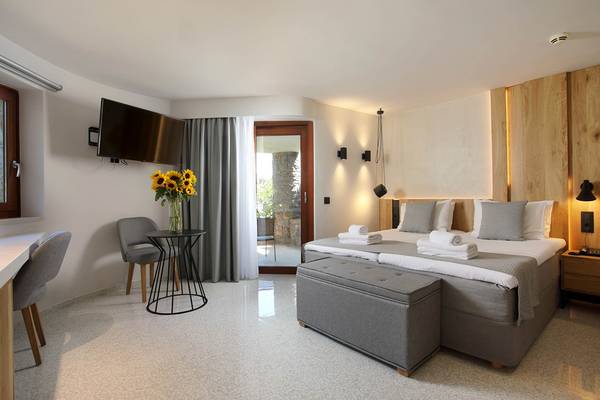 Innenansicht eines Zimmers im Ikaros Beach Luxury Resort & Spa mit einem Bett, Sonnenblumen, Fernseher und modernem Interieur.