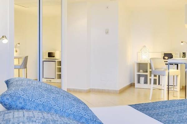 Weißes Zimmer im Tropic Garden Hotel Apartments mit Bett, Stühlen und Schreibtisch.