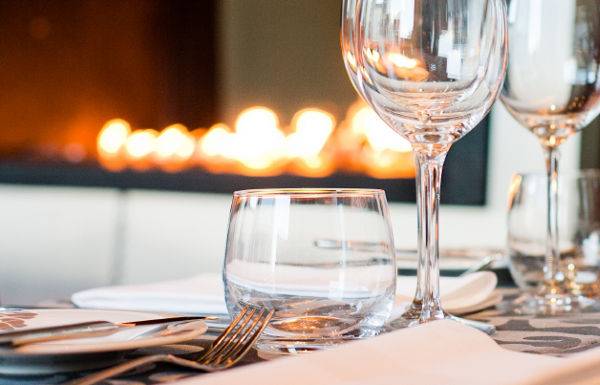 Ein Tisch im Restaurant des Radisson Blu Resort & Spa, Cesme, ist gedeckt mit Gläsern, Besteck und Servietten, vor einem offenen Kamin.