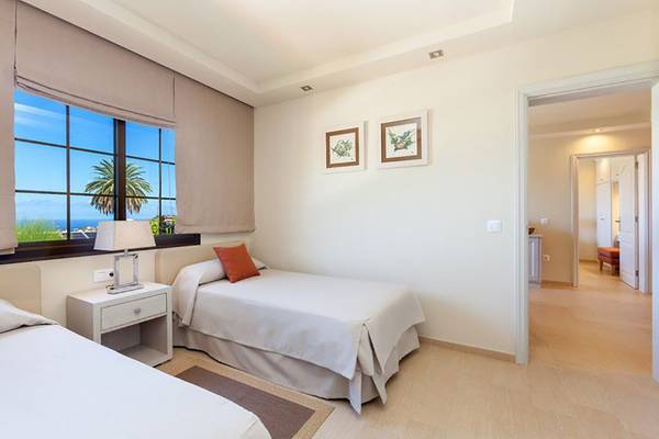 Zweibettzimmer im Ambassador Apartments mit Meerblick, weißen Wänden, zwei Betten, Nachttischen und offenem Eingang.