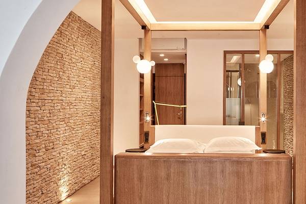 Schlafzimmer im Myconian Naia Hotel mit Holzbett und weißen Kissen, umgeben von Steinwänden.