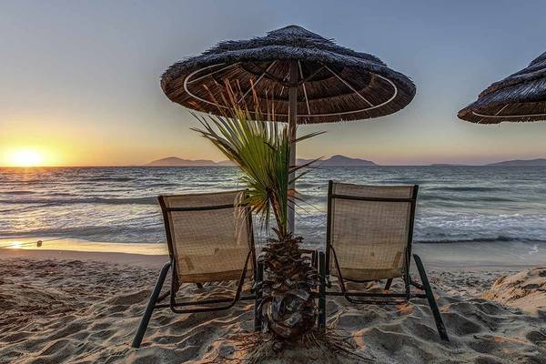 Sonnenuntergang am Strand mit zwei Liegen und einer Palme im Vordergrund.
