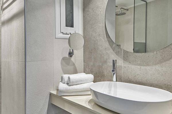 Badezimmer im Atlantica Marmari Palace mit grauen Fliesen, einem runden Spiegel und einem Waschbecken.