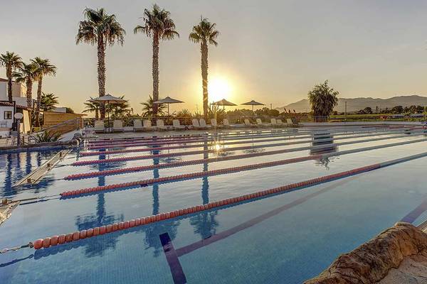Schwimmbecken des Atlantica Marmari Palace bei Sonnenuntergang mit Palmen und Sonnenschirmen