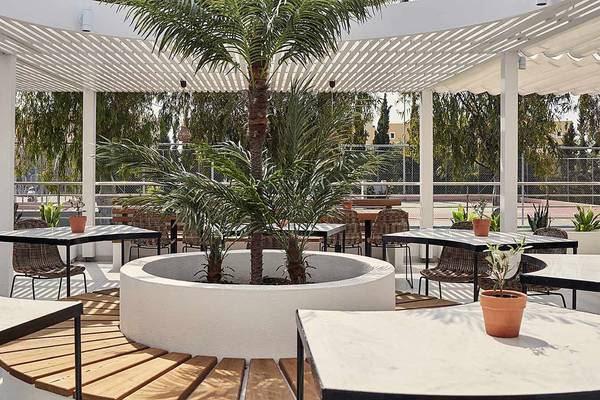 Im Freien gelegenes Restaurant des Atlantica Marmari Palace Hotels mit Tischen, Stühlen und einer großen Palme in der Mitte.
