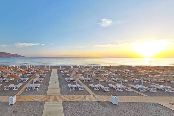 Strand des Anemos Luxury Grand Resort bei Sonnenuntergang mit vielen Liegen und Sonnenschirmen