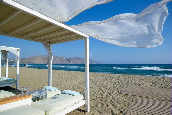 Strand-Lounge-Bereich im Anemos Luxury Grand Resort mit weißen Liegen und Sonnenschirmen.