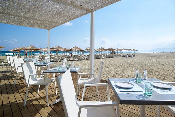 Restaurant im Anemos Luxury Grand Resort mit Blick auf den Strand und weiße Stühle und Tische