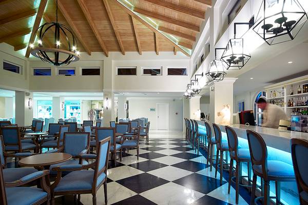 Hotellobbybereich des Anemos Luxury Grand Resort mit schwarz-weißem Schachbrettboden und Bar.