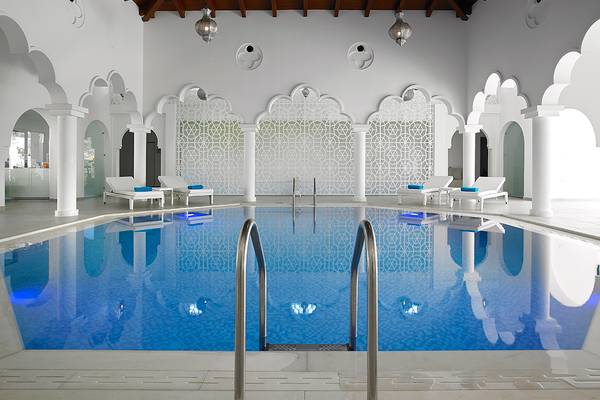 Innenpool des Anemos Luxury Grand Resort mit weißen Wänden und Mustern, umgeben von Loungestühlen.