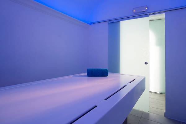 Massageraum im Anemos Luxury Grand Resort mit weißem Tisch und blauer Beleuchtung.