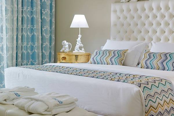 Luxuriöses Bettzimmer im Anemos Luxury Grand Resort mit weißen Möbeln, blauen Vorhängen und gemusterter Bettwäsche.