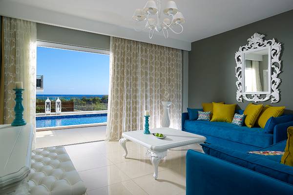 Wohnzimmer mit Poolblick im Anemos Luxury Grand Resort mit blauen Sofas, weißem Tisch und Meersicht.