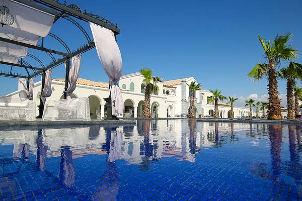 Außenpool im Anemos Luxury Grand Resort mit weißen Gebäuden und Palmen im Hintergrund.