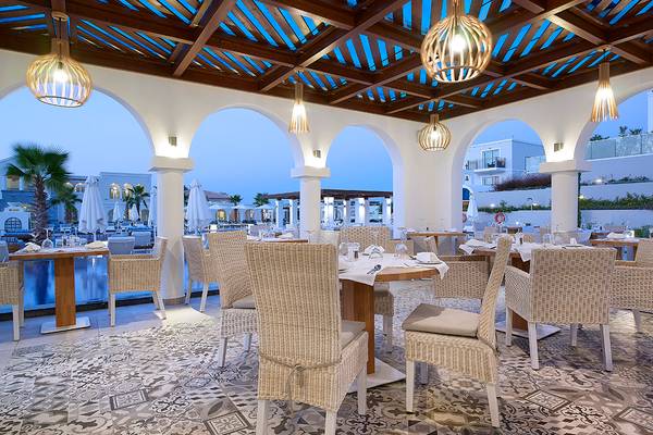 Innenbereich des Anemos Luxury Grand Resort Restaurants mit Tisch, Stühlen und dekorativen Lampen.