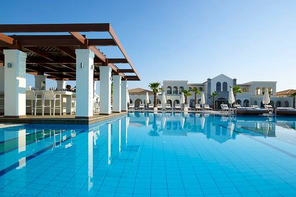 Pool im Anemos Luxury Grand Resort mit Sonnenliegen und Palmen.