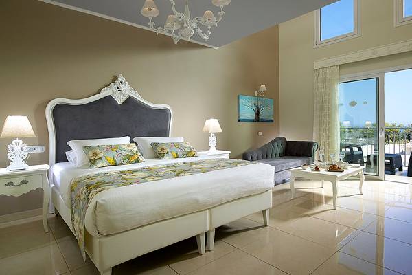 Schlafzimmer im Anemos Luxury Grand Resort mit Bett, Nachttischen und Balkonzugang.