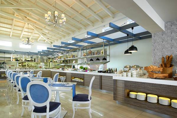 Innenansicht des Restaurants im Anemos Luxury Grand Resort mit weißen Tischen und Stühlen.