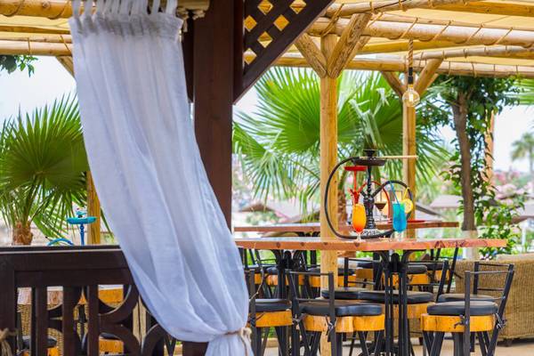 Terrasse des Cavo Maris Beach Hotels mit Tischen und Stühlen unter einem Pavillon.
