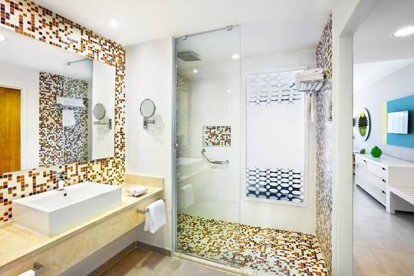Badezimmer im Playa Vista Azul Hotel in Varadero mit gefliester Wand, Dusche und Waschbecken.
