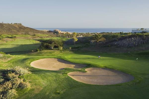 Golfplatz mit Blick auf das Meer und Palmen im Hintergrund.