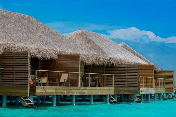 Cocoon Maldives Wasserbungalows mit Blick auf das Meer und eine Person, die im Wasser schwimmt.