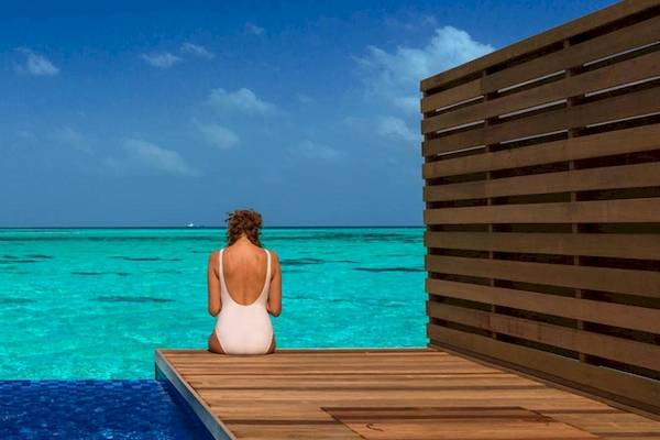 Frau im weißen Kleid sitzt am Rand des Infinity-Pools im Cocoon Maldives