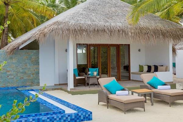 Außenbereich des Cocoon Maldives Hotels mit einer kleinen Hütte, zwei Liegestühlen und einem Pool.