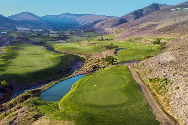 Luftaufnahme eines Golfplatzes im Bergland mit Wasserhindernis und üppiger Vegetation.