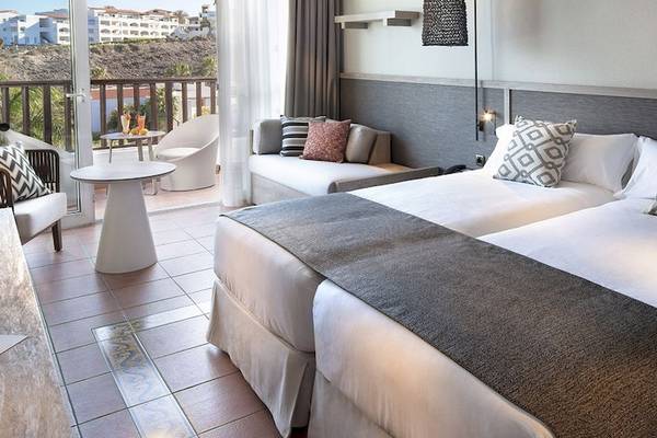 Doppelzimmer im Fuerteventura Princess Hotel mit Balkon, zwei Betten, Tisch und Aussicht auf die Stadt.