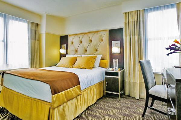 Schlafzimmer im The New Yorker Hotel mit einem großen Bett, gelben Kissen und einer modernen Einrichtung.