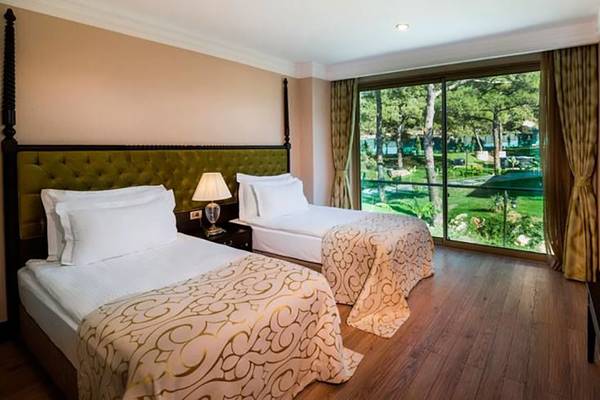 Doppelzimmer im Vogue Hotel Supreme Bodrum mit zwei Betten, Glasfenstern und Gartenblick.
