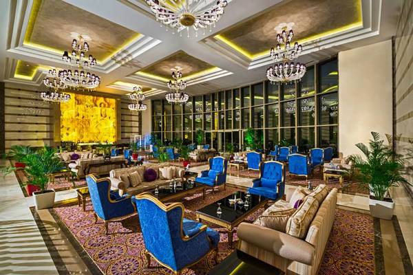 Lobby des Vogue Hotel Supreme Bodrum mit blauen Stühlen, goldenen Kronleuchtern und großen Fenstern.