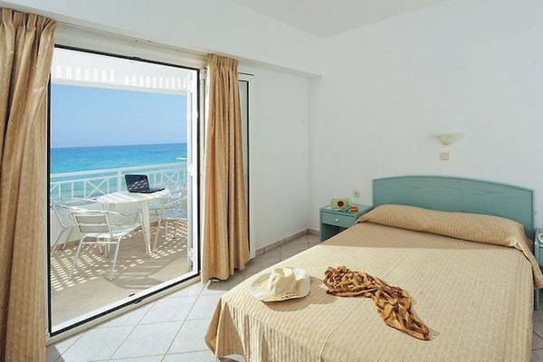 Zimmer im Ariadne Beach Hotel mit Balkon und Meerblick, einschließlich eines Bettes, eines Tisches und eines Laptop auf dem Balkon.