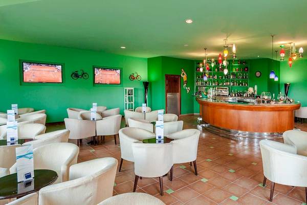 Cocktail-Bar im Occidental Jandia Royal Level Hotel mit grünen Wänden, weißen Stühlen und einer Theke.