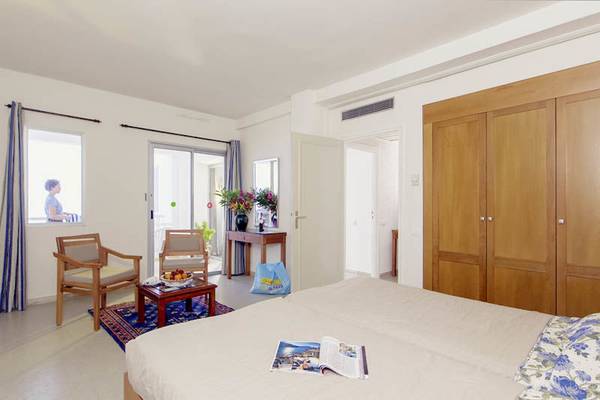 Interieur eines Zimmers im Calimera Yati Beach Hotel mit Bett, Möbeln, Fenster und Blick auf den Garten.
