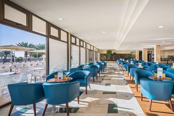 Innenbereich des Occidental Jandia Mar Hotels mit vielen blauen Stühlen und Tischen, große Fenster und Sonnenschirme draußen