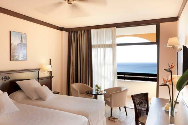 Zweibettzimmer im Occidental Jandia Royal Level mit Meerblick, zwei Betten, Sesseln, Schreibtisch und Aussicht auf das Meer.