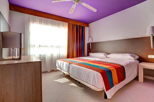 Doppelbettzimmer im SBH Monica Beach Resort mit bunter Bettdecke und weißen Kissen.