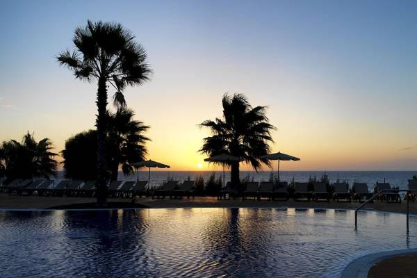 Sonnenuntergang am Pool des H10 Tindaya Hotels mit Palmen und Sonnenschirmen.