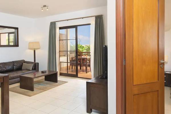 Innenansicht der Suite im Melia Tortuga Beach Hotel mit Wohnzimmer, Couch, Tisch, Lampe, Fernseher und Balkon.