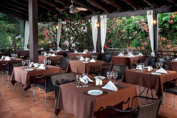 Restaurant-Terrasse des Melia Tortuga Beach Hotels mit braunen Tischen und Stühlen, umgeben von Pflanzen.