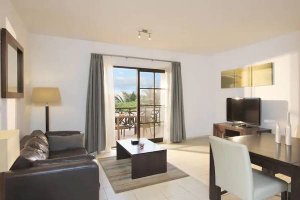 Wohnbereich des Melia Tortuga Beach Hotels mit Couch, Tisch, Fernseher und Balkonzugang