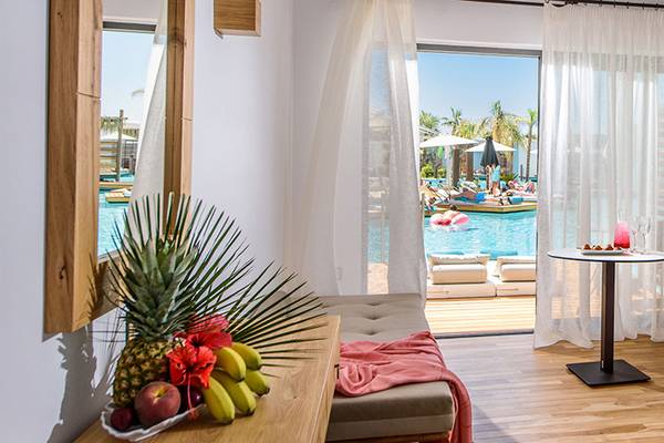 Innenansicht eines Zimmers im Stella Island Luxury Resort & Spa Hotel mit Blick auf den Pool und tropischen Früchten auf dem Tisch.