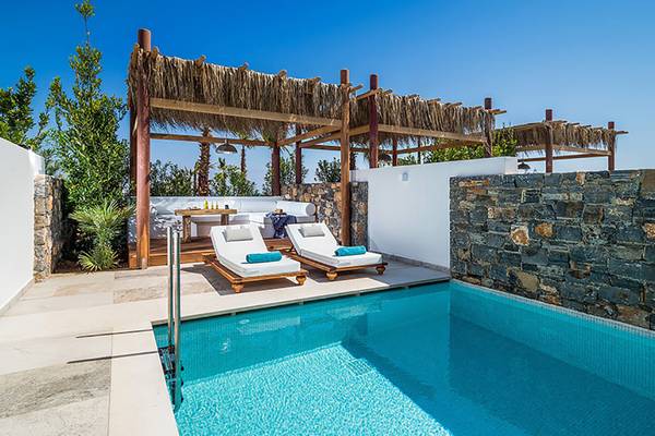 Außenpoolbereich mit zwei Liegen und einem Tisch unter einem Strohdach im Stella Island Luxury Resort & Spa