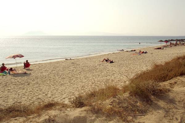 Leute, die am Strand sonnenbaden, mit Sonnenschirmen und Bergen im Hintergrund.