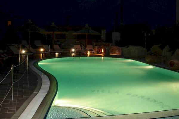 Der Pool der Villa Romantica ist bei Nacht mit blauer Beleuchtung und Sonnenliegen drumherum zu sehen.